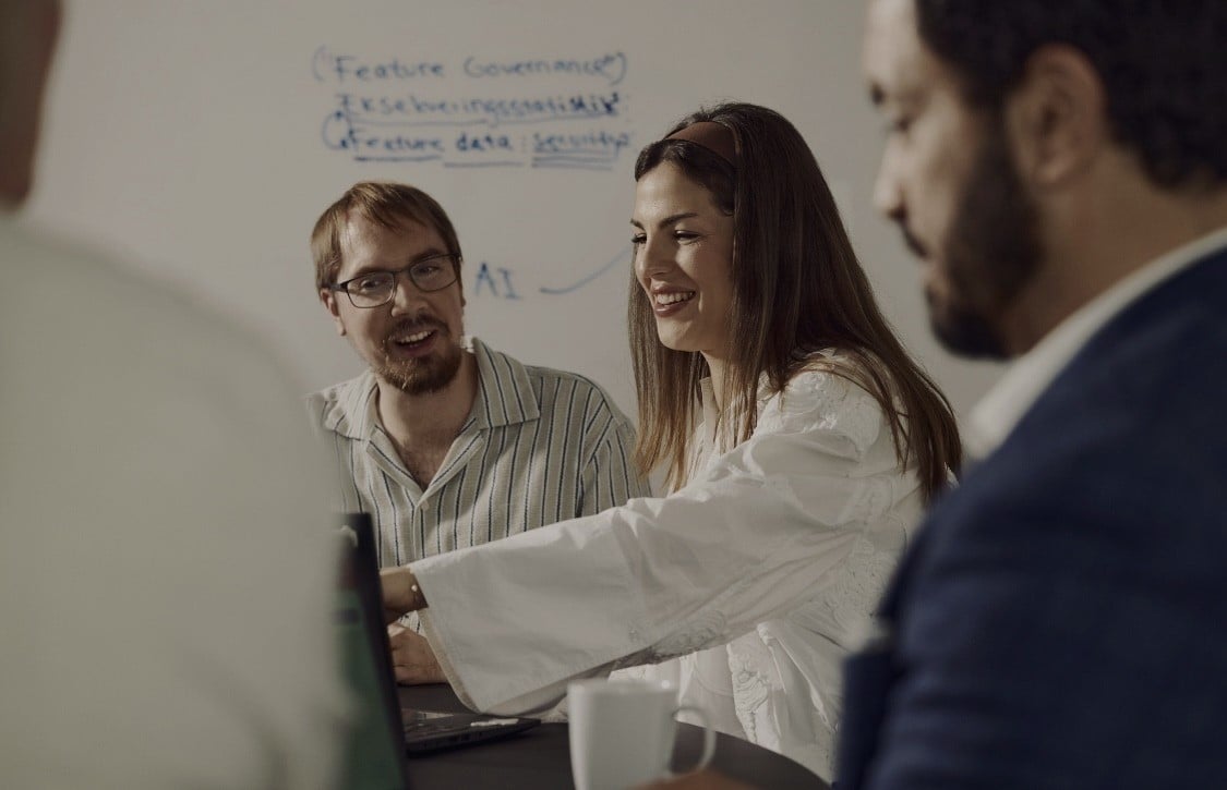 Tre personer diskuterer ved whiteboard med notater om feature governance og data struktur.